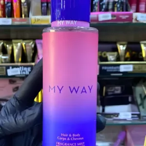 Main gantée présentant le flacon dégradé rose et bleu de la brume My Way pour corps et cheveux, sur une étagère de produits.