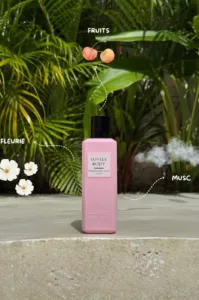 Flacon rose Lovely Body entouré d'icônes de cerises, fleurs blanches et nuage de musc sur fond tropical.