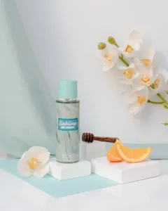 Brume parfumée Rimita Sublime and Radiant!, flacon turquoise entouré d’orchidées blanches, miel et tranches d’orange.