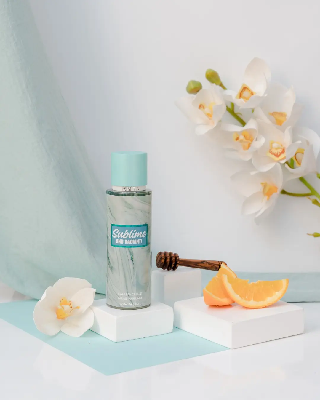 Brume Rimita Sublime and Radiant! (200 ml) – Fraîcheur & éclat Brume parfumée Rimita Sublime and Radiant!, flacon turquoise entouré d’orchidées blanches, miel et tranches d’orange.