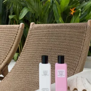Brumes de luxe Coco Shine et Lovely Body posées sur un rebord blanc avec coquillage devant des chaises longues en osier.