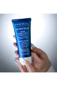 Tube bleu de crème hydratante Phyteal Atopicrème pour peaux sensibles, tenu par des mains aux ongles soignés sur fond clair.