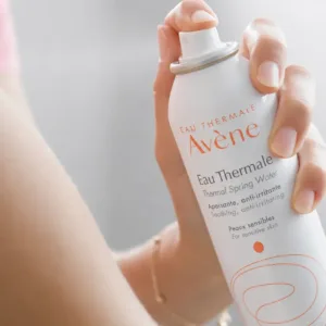 Une main tenant un spray d'Eau Thermale Avène pour peaux sensibles, prêt à être vaporisé sur le visage.