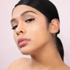 Femme avec maquillage lumineux, fard à paupières pailleté, lèvres roses, teint éclatant, possiblement Flormar Highlighter Illuminator N°002.