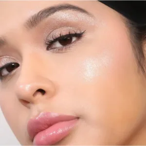 Gros plan sur un visage maquillé avec highlighter, fard à paupières scintillant, eyeliner et lèvres roses brillantes, possiblement Flormar Highlighter Illuminator N°002.