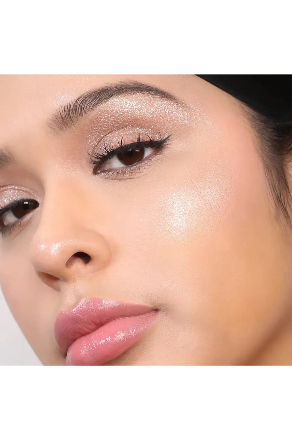 Maquillage Lumineux : Gros Plan Éclatant Gros plan sur un visage maquillé avec highlighter, fard à paupières scintillant, eyeliner et lèvres roses brillantes, possiblement Flormar Highlighter Illuminator N°002.