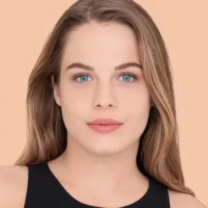 Portrait d'une femme souriante, teint lumineux et yeux bleus. Elle porte le correcteur Maybelline Fit Me n°15 pour unifier son teint.