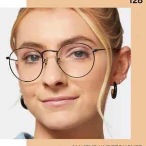 Gros plan sur une femme blonde aux yeux bleus portant des lunettes. Son teint est sublimé par le fond de teint Maybelline Fit Me! teinte 128.