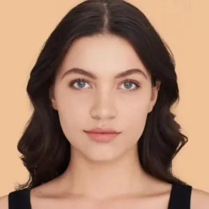 Gros plan d'une jeune femme aux cheveux foncés et yeux bleus. Son teint est unifié, lisse et mat, résultat du fond de teint Maybelline Fit Me! 128.
