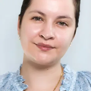Portrait de femme souriante, peau nue sans maquillage, cheveux courts, vêtue d'un chemisier bleu à volants.