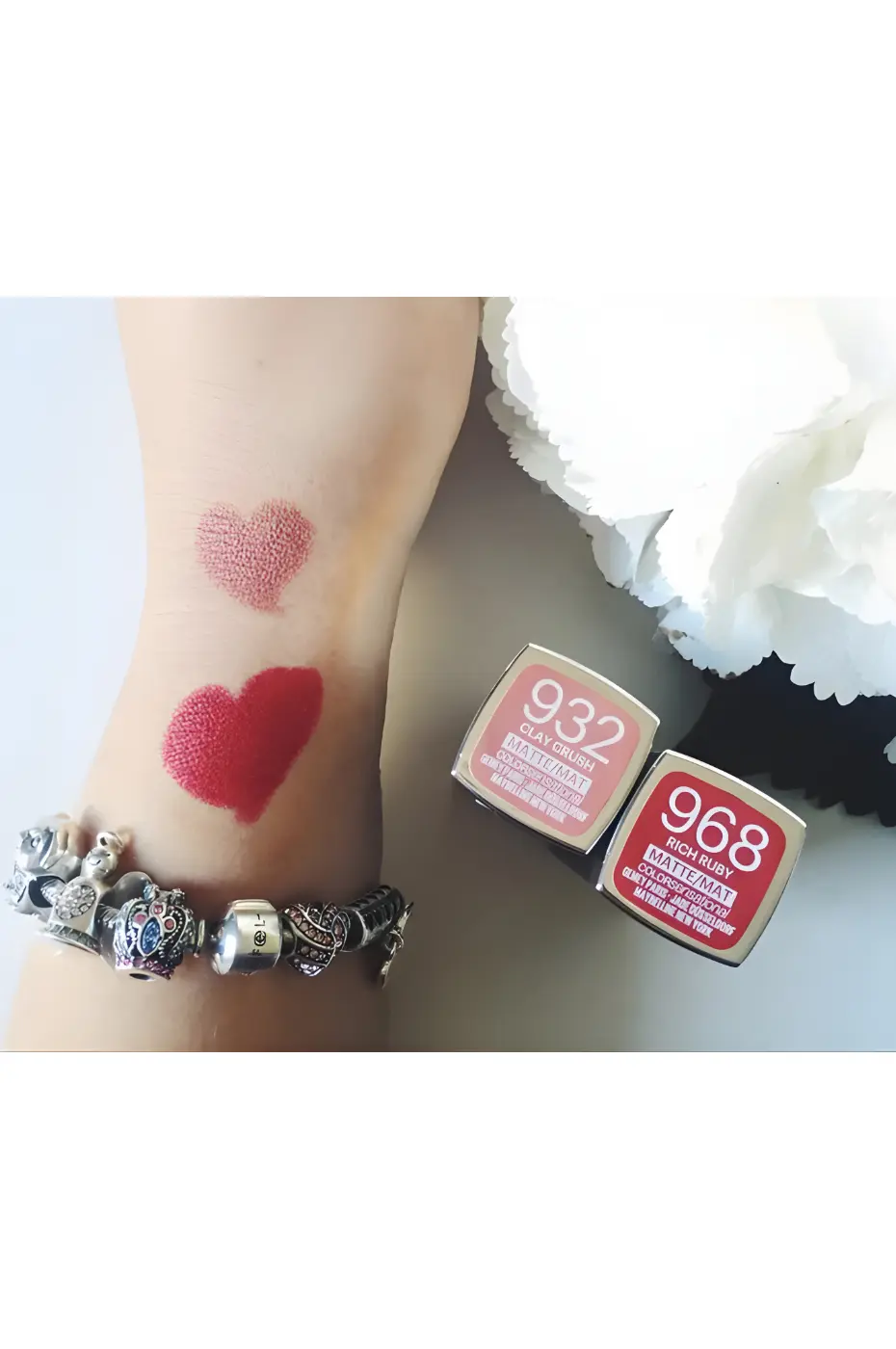 Swatches Maybelline : Cœurs de Couleur Mat N°932 & N°968 Deux cœurs de rouge à lèvres mats (rose poudré et rouge intense) sur un bras portant un bracelet Pandora, à côté de leurs packagings.