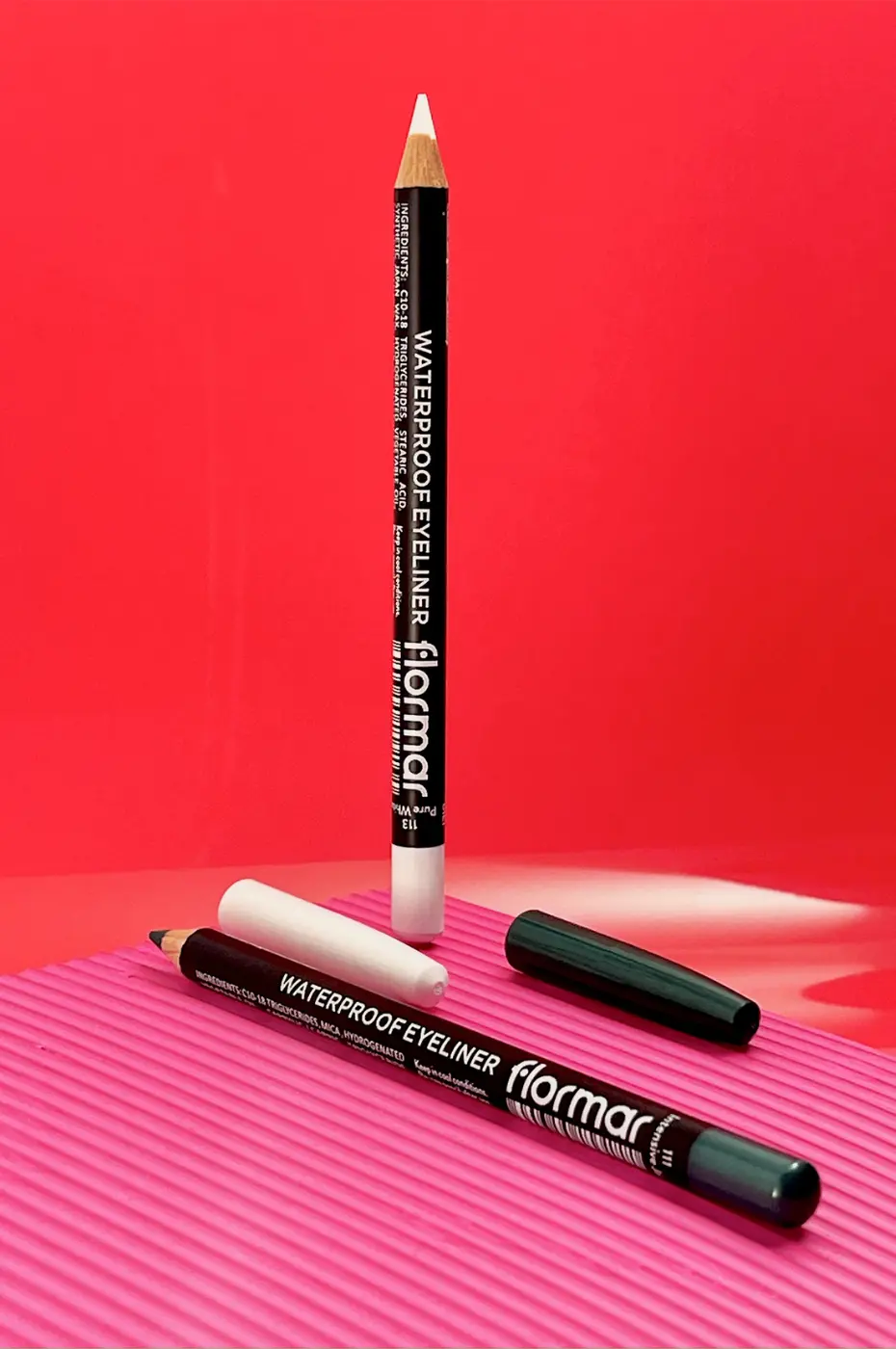 Duo de Crayons Eyeliner Flormar Waterproof – Blanc & Foncé Deux crayons eyeliner Flormar Waterproof $\text{N}^\circ 113$ blanc et foncé, posés sur un fond rose vif texturé.