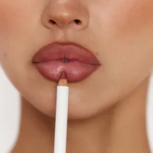 Gros plan sur une femme appliquant un crayon à lèvres couleur rose antique sur sa lèvre inférieure pour un contouring discret.