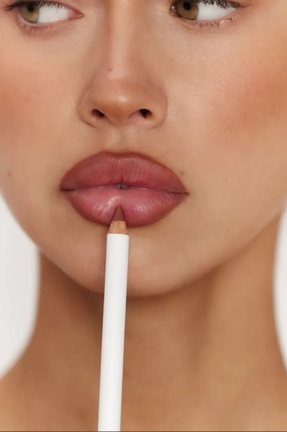 Couleur Nude et Rose Antique Gros plan sur une femme appliquant un crayon à lèvres couleur rose antique sur sa lèvre inférieure pour un contouring discret.