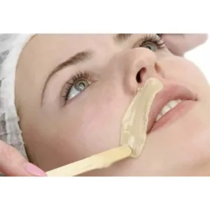 Femme recevant une épilation de la lèvre supérieure avec de la cire chaude appliquée par une esthéticienne.