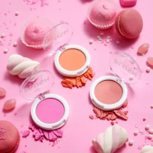 Trois boîtiers de blush HEAN BLUSH BABY (rose vif, corail, rose pêche) entourés de macarons, guimauves et bonbons sur un fond rose.