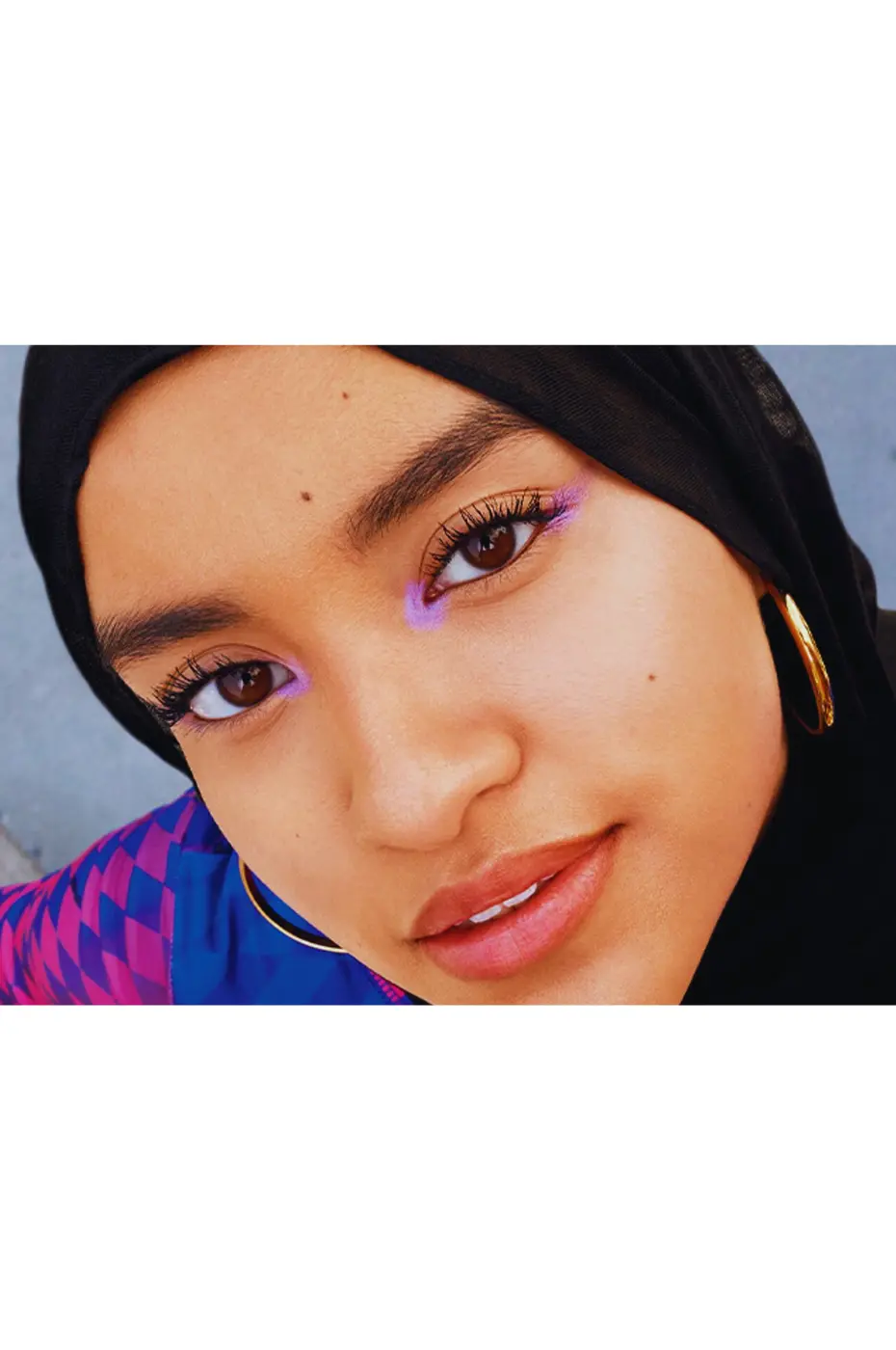 Le Chic Flottant : Eye-liner Lilas et Style Moderne Portrait d'une jeune femme portant un hijab noir et un eye-liner flottant lilas vif sur les yeux. Grosses boucles d'oreilles dorées.