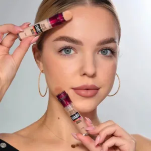 Mannequin aux yeux bleus tenant deux tubes du correcteur Maybelline Instant Age Rewind Eraser Concealer.