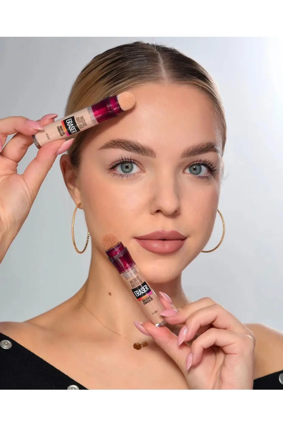 Mannequin avec Correcteur Maybelline Instant Anti-Âge Mannequin aux yeux bleus tenant deux tubes du correcteur Maybelline Instant Age Rewind Eraser Concealer.