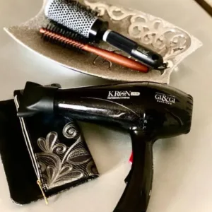 Sèche-cheveux Gi&Gi KRON plus noir posé à côté d'une trousse et d'un plat contenant une brosse ronde et une brosse plate.