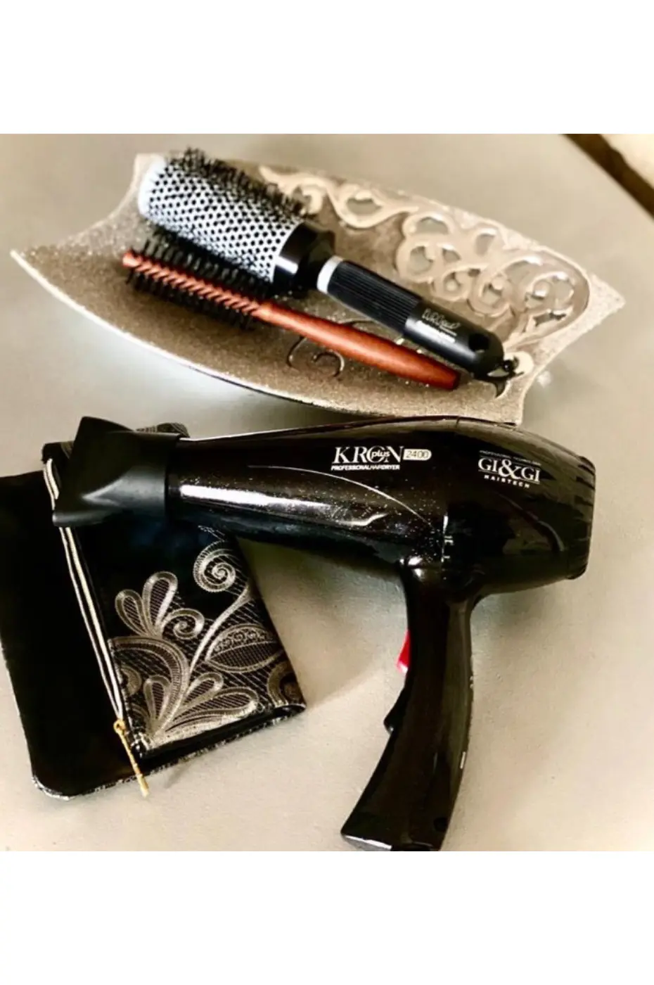 Sèche-cheveux Gi&Gi Sèche-cheveux Gi&Gi KRON plus noir posé à côté d'une trousse et d'un plat contenant une brosse ronde et une brosse plate.