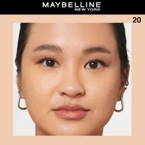 Gros plan d'une femme portant le correcteur Maybelline Fit Me teinte N°20 pour un teint unifié. Elle porte des boucles d'oreilles dorées.
