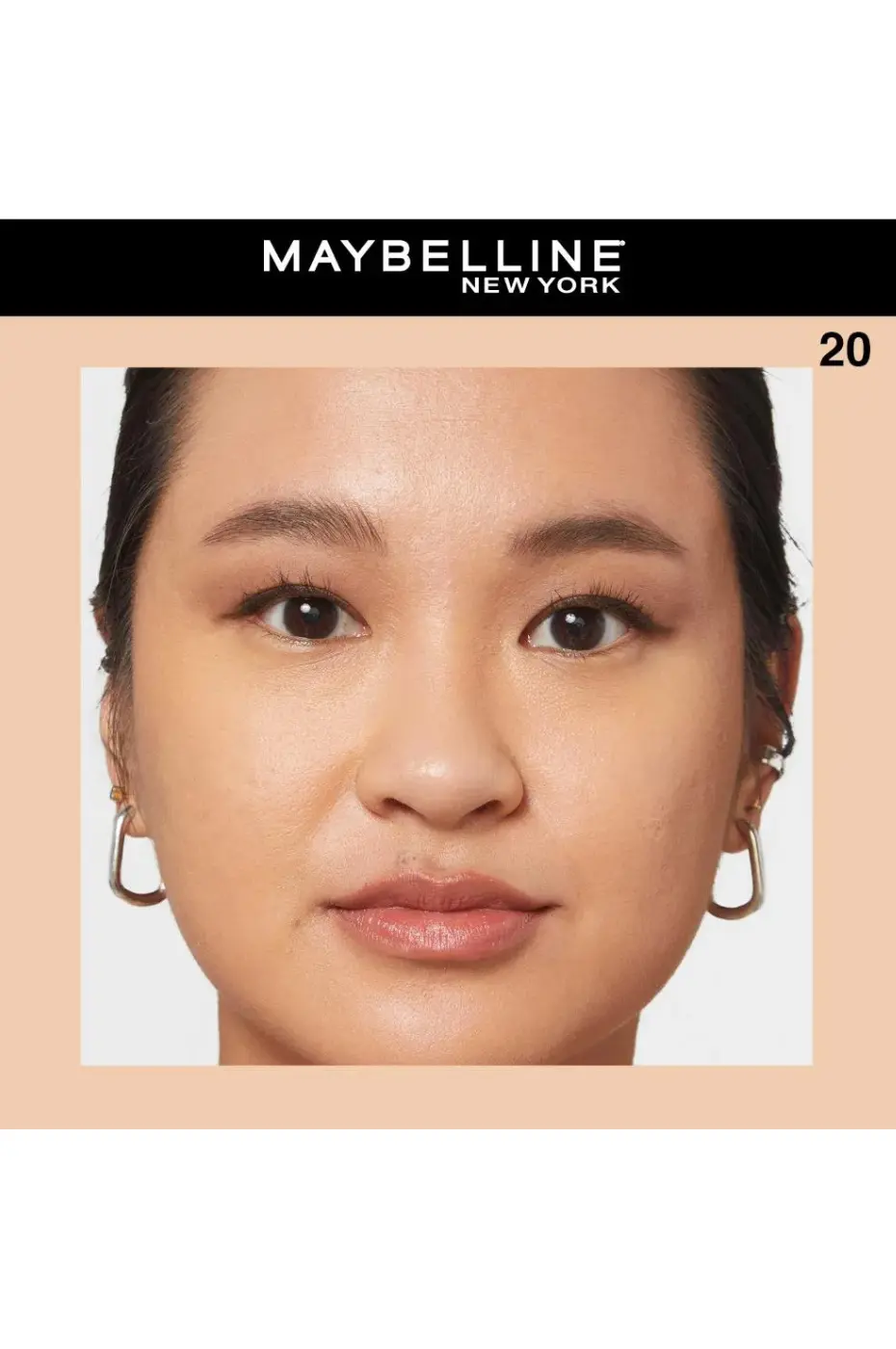 Teint Parfait N°20 : L’Éclat Naturel Fit Me Gros plan d'une femme portant le correcteur Maybelline Fit Me teinte N°20 pour un teint unifié. Elle porte des boucles d'oreilles dorées.