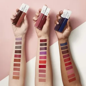 Nuancier de bras Super Stay Matte Ink Maybelline sur trois carnations. Teintes nudes, rouges, prunes et bleues avec tubes en main.