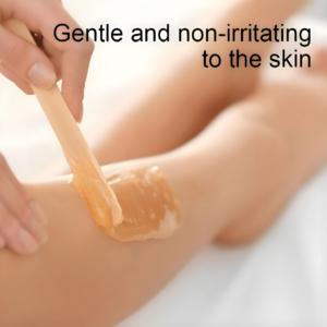 Gros plan d'étalement de cire ambrée sur la jambe. Spatule bois hypoallergénique pour peau sensible et épilation sans douleur.