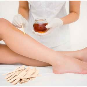 Esthéticienne appliquant de la cire sur une jambe avec une spatule fine. Lot de 50 bâtonnets en bois au premier plan.