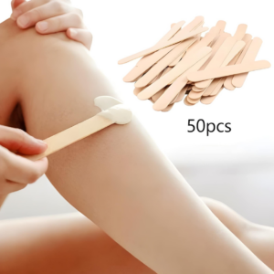 Application de cire avec une spatule en bois sur une jambe. Lot de 50 applicateurs naturels pour une épilation précise.