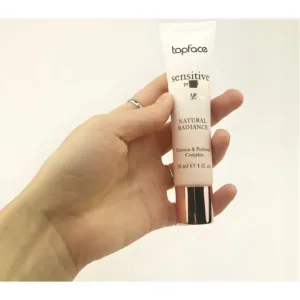 Main tenant un tube de base illuminatrice Topface Sensitive Mineral Natural Radiance sur un fond blanc épuré.
