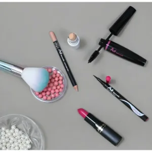 Assortiment de maquillage AS Kozmetik : mascara, rouge à lèvres, eyeliner et perles de teint sur fond gris.