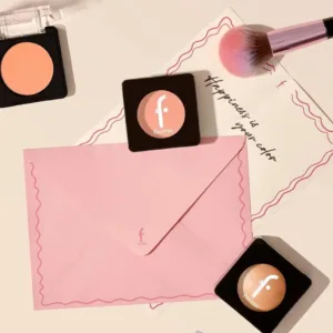 Mise en scène de boîtiers de blush Flormar avec un pinceau de maquillage et une enveloppe rose sur un fond beige pastel.