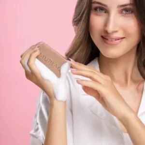 Jeune femme souriante utilisant le savon exfoliant Muriac Lightact pour un teint frais et lumineux.