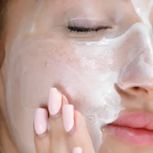 Gros plan sur l'application du gel-crème nettoyant K-REINE, texture onctueuse blanche sur la joue et le menton d'une femme.