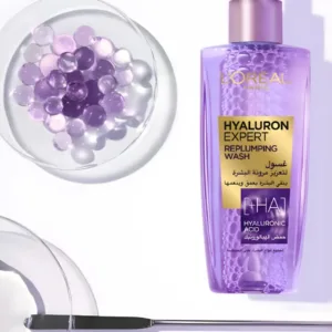 Flacon pompe violet de gel nettoyant Hyaluron Expert à l'acide hyaluronique, posé à côté de perles d'eau et de gel.