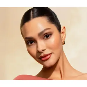 Portrait d'une femme au teint lumineux portant un blush pêche naturel sur les pommettes et un maquillage élégant et sobre.