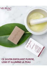 Savon exfoliant Muriac Lightact sur une feuille verte à côté d'un mortier d'huile d'argan et de sa boîte d'emballage.