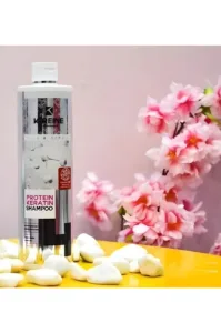 Flacon de shampoing K-Reine Protein Keratin sur table jaune avec galets blancs et fleurs de cerisier roses en fond.