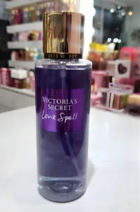 Flacon de brume parfumée Love Spell Victoria's Secret violet avec bouchon doré posé sur un comptoir blanc de parfumerie.
