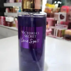 Flacon de brume parfumée Love Spell Victoria's Secret violet avec bouchon doré posé sur un comptoir blanc de parfumerie.