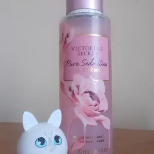 Photo réelle de la brume Victoria's Secret La Crème posée sur un meuble en bois à côté d'un petit baume en forme de chat.