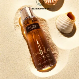 Brume Vanilla Lace de Victoria's Secret posée sur du sable fin avec des coquillages, sous une lumière chaude d'été.