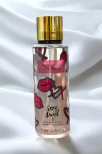 Flacon transparent Brume Victoria's Secret Sexy Angel décoré de lèvres et cœurs roses, bouchon doré sur fond blanc drapé.
