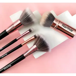 Assortiment de pinceaux de maquillage Flormar rose doré et noir sur un socle géométrique et fond rose.