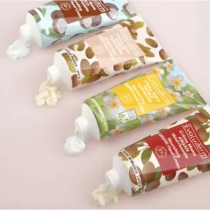 Quatre tubes de crèmes mains Evoluderm (Coco, Karité, Monoï, Argan) avec leur texture onctueuse sur un fond rose pâle.
