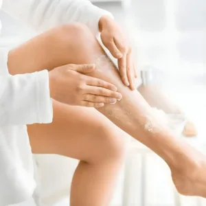 Femme appliquant le gommage Evoluderm sur ses jambes par mouvements circulaires pour exfolier la peau en douceur.