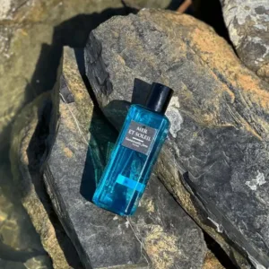 Flacon de parfum bleu Emmanuelle Jane Mer et Soleil posé sur des rochers de bord de mer, exposé au soleil.