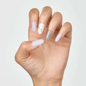 Manucure avec faux ongles amande violets mat, un ongle motif marbre blanc et un ongle pailleté argenté sur fond blanc.